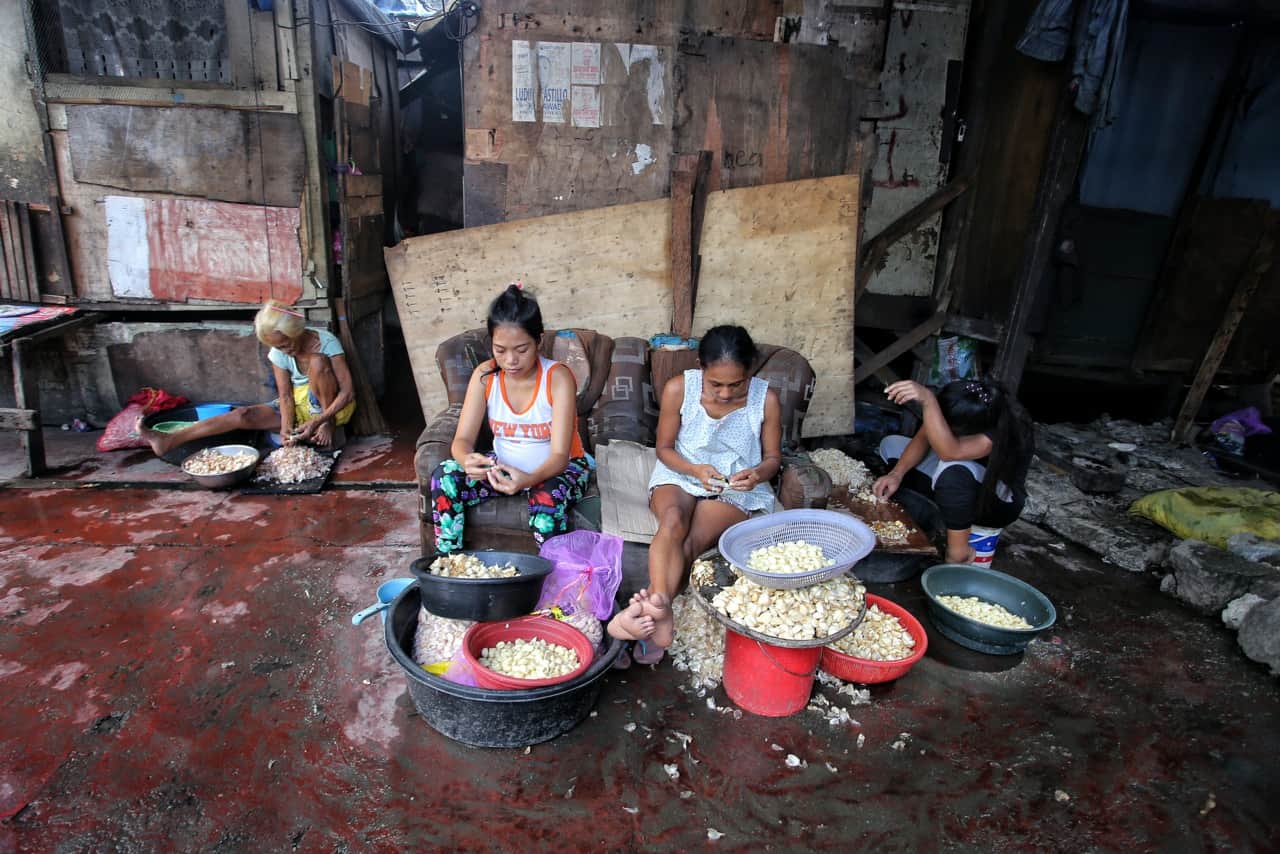 Happy Land slum in Manila is below sea level and floods frequently. Still, work goes on. The few pesos these women earn from peeling and selling garlic will help with essentials  like electricity, food, bottled water and school fees for their children.